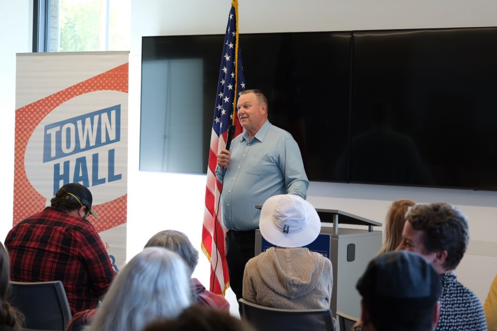 Tester speaking into a microphone at his Bozeman town hall.